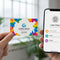 Custom printed white plastic business card held near smartphone displaying digital contact info.