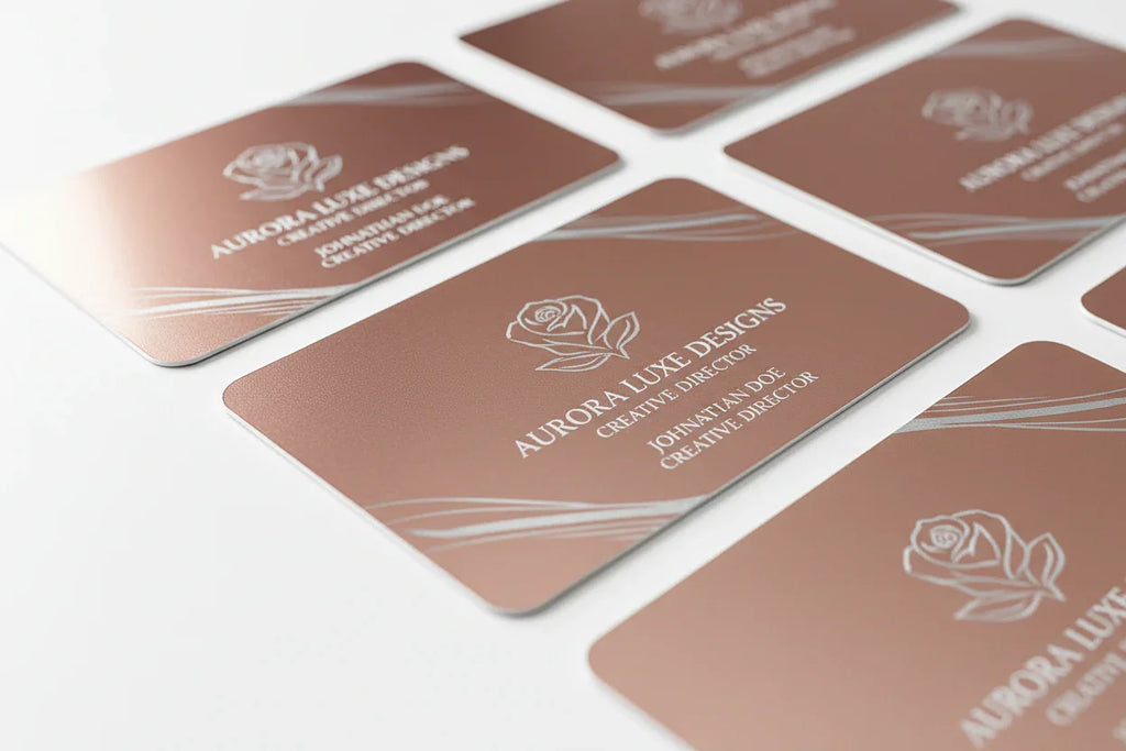 Rose gold plastic business cards with silver printing and rounded corners on white background